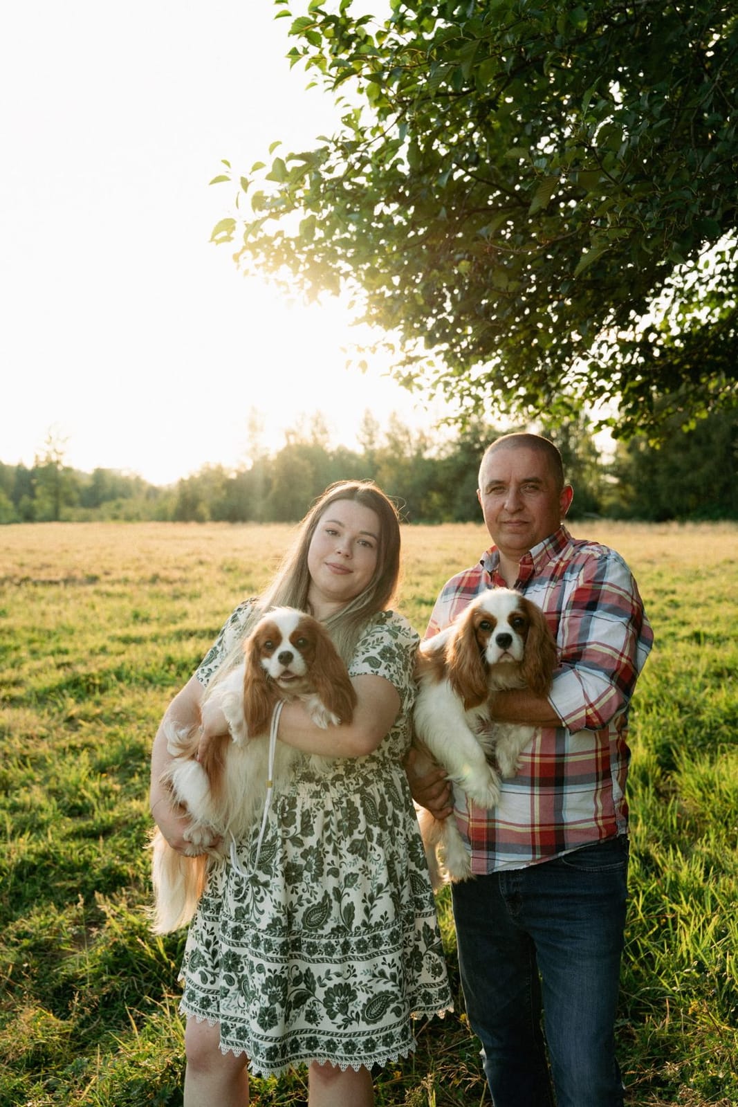 Laura and Eugene holding two Blenheim Cavaliers in a sunny field